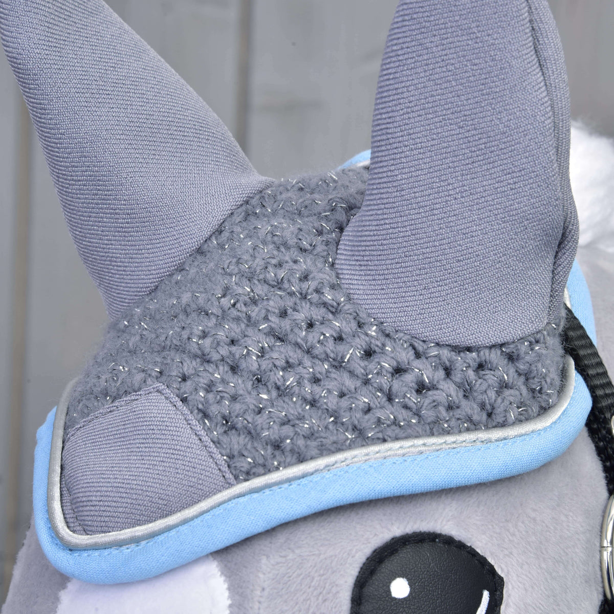 Close-up of the Ear bonnet crocheted grey on a Hobby Horse: sparkly crochet stitches, grey ears, blue and silver edging