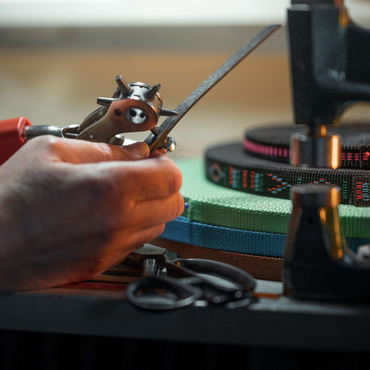 Detail from the workshop: a rotary hole punch, a black strap, scissors and rolls of patterned webbing