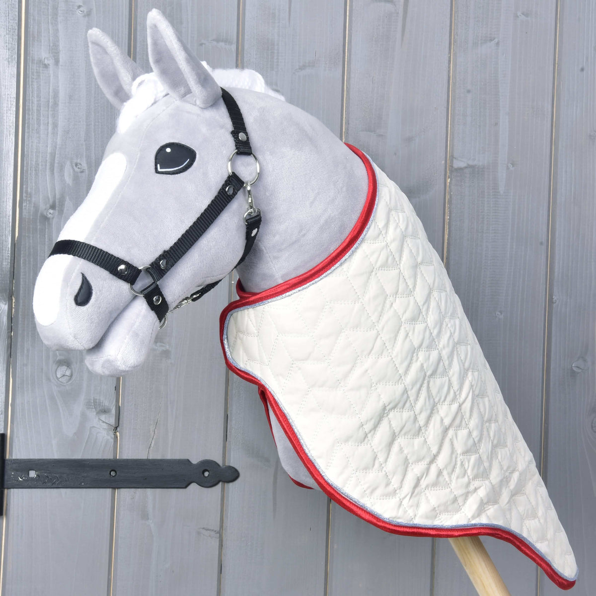 Szürke Hobby Horse ló fekete kötőfékben, a nyakán krémszínű steppelt szállítótakaró piros szegéllyel