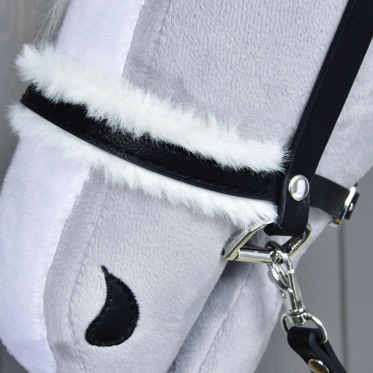 Close-up of the black noseband lined with fluffy white fur, with a silver ring and the snap hook of the reins