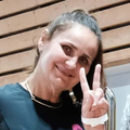 Smiling LarDen Hobby Horse maker with a dark ponytail showing a peace sign in front of a wooden slatted wall