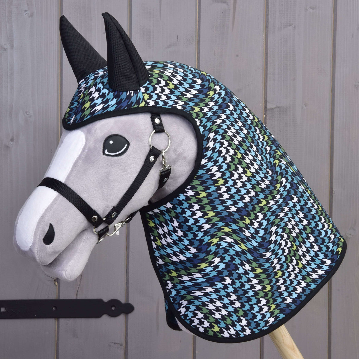Szürke Hobby Horse ló fekete kötőfékkel, rajta a Lara esőtakaró, amelynek tyúklábmintás, fekete fülű kapucnija a fejet is takarja