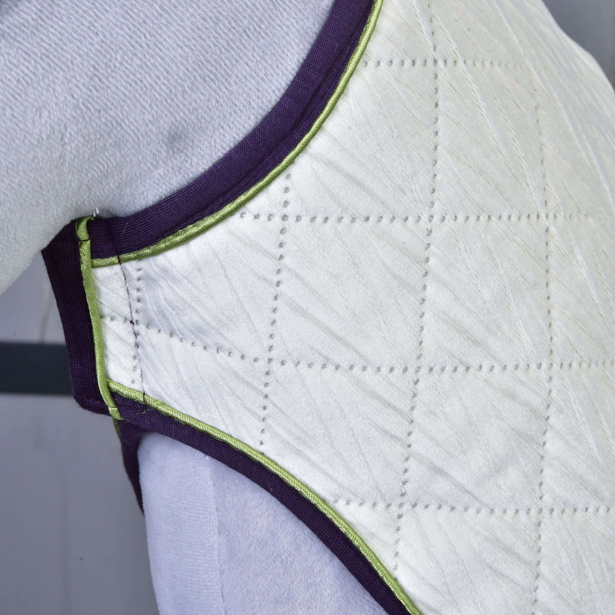 Set Leonardo blanket on a grey Hobby Horse up close: ivory diamond quilting with leaf texture, lime piping, purple binding