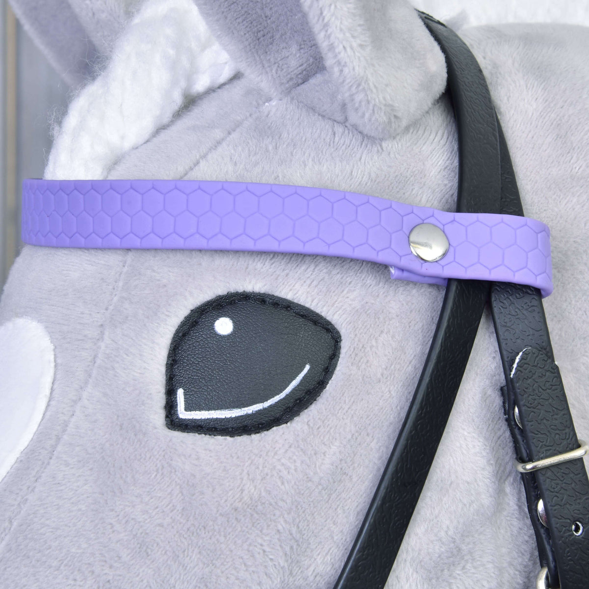 A világoslila méhsejtmintás homlokszíj közelről ezüst szegeccsel és fekete pofaszíjjal egy szürke Hobby Horse lovon