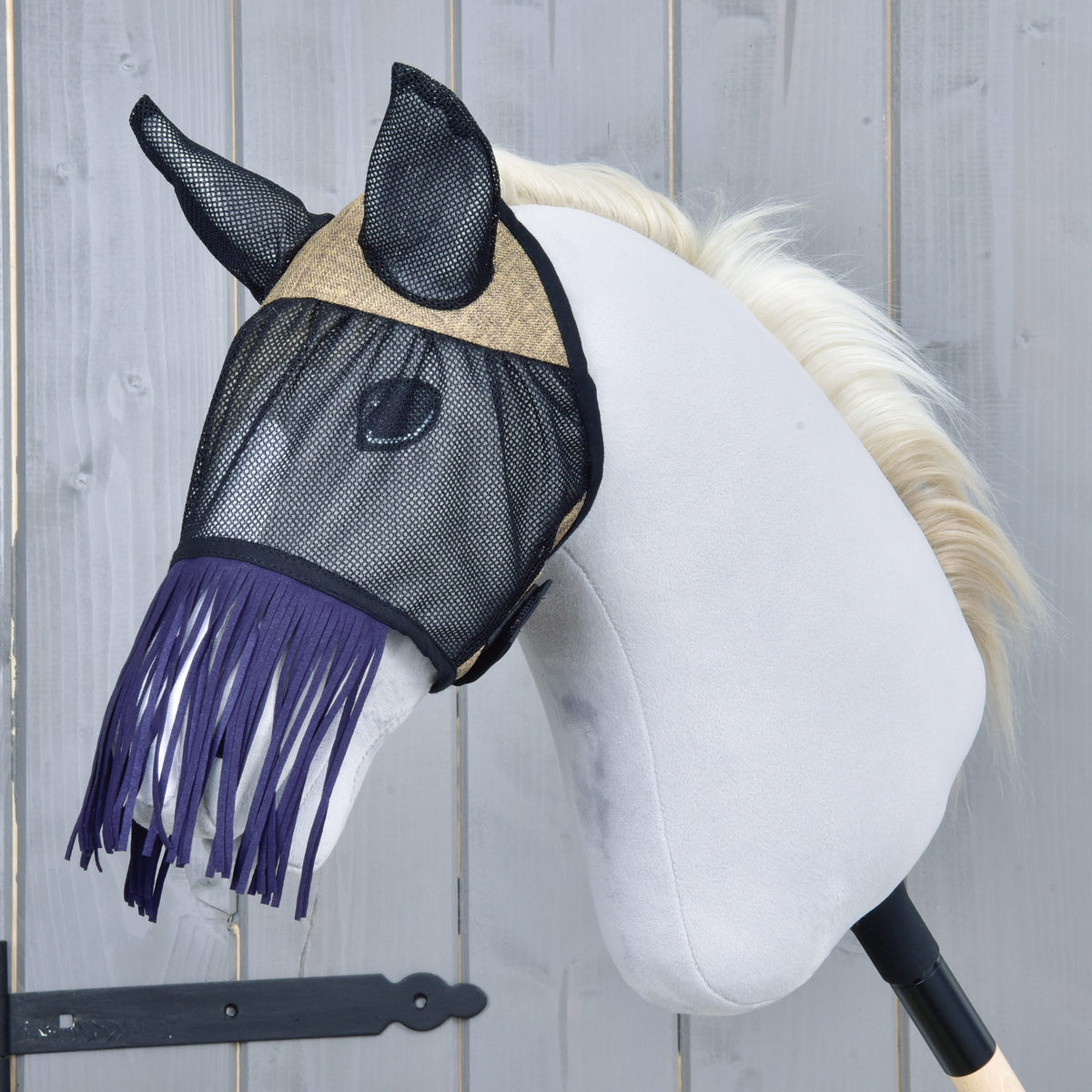 LarDen Fly Mask De Luxe Mona in black mesh with a beige woven brow panel and dark purple nose fringe on a grey Hobby Horse