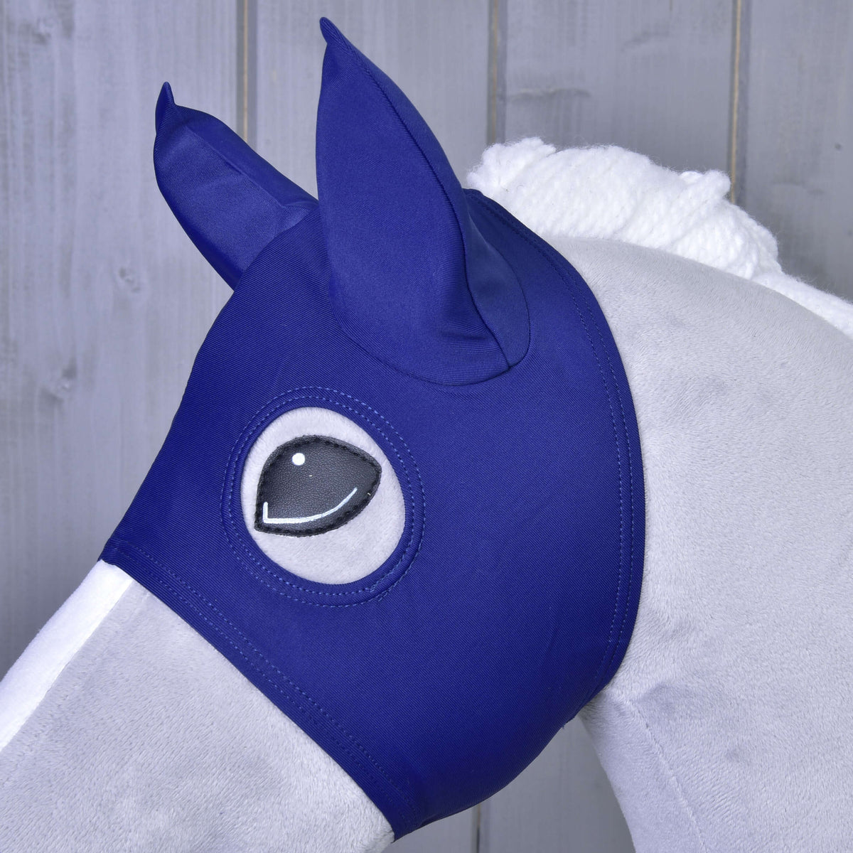 Close-up of the Horse Mask with navy fabric ear covers on a grey Hobby Horse, the black eye framed by the opening