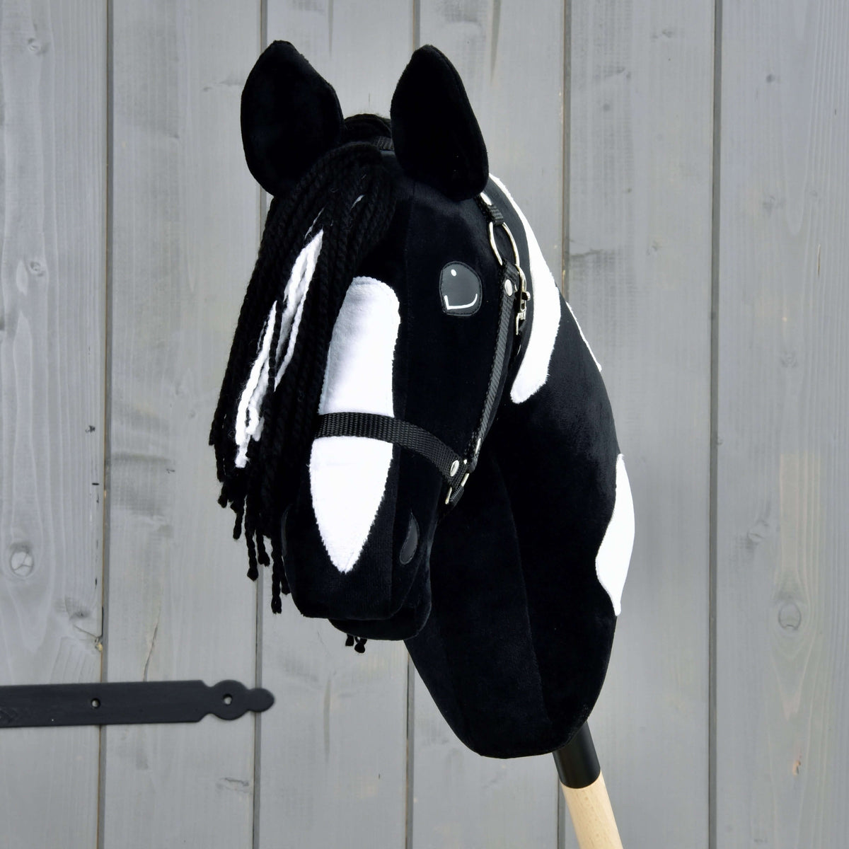 Hobby Horse Merlin fekete kötőfékkel elölről: fehér szálakkal tarkított fekete fonalüstök egy széles fehér hóka fölött