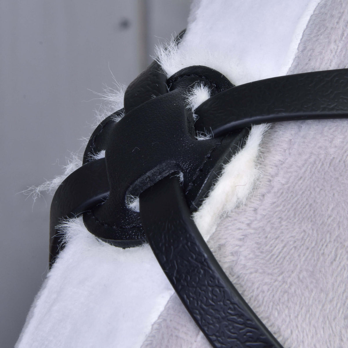 Angled close-up of the Mexico noseband's padded crossing point, black leatherette straps over white fleece on a Hobby Horse