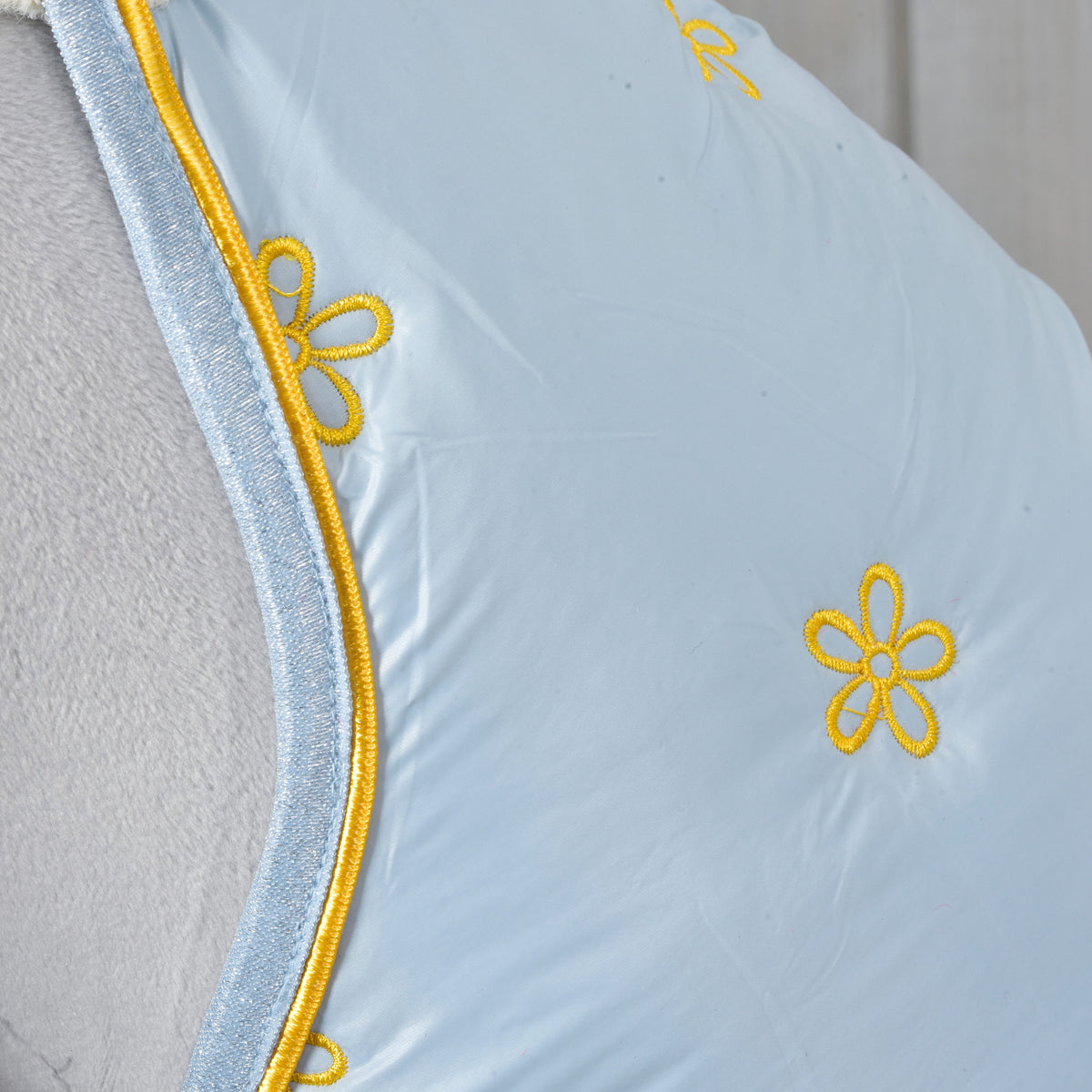Detail of yellow embroidered daisies and piped edge on the pale blue Hobby Horse Stable Blanket Misty over grey plush