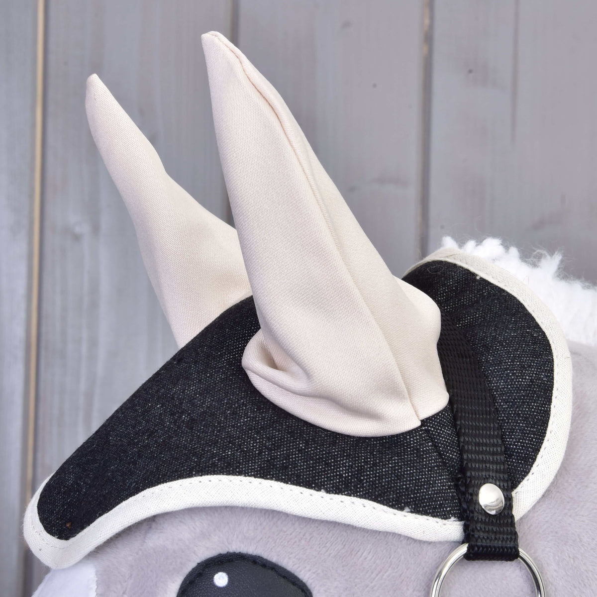 Close-up of the dark denim ear bonnet with tall cream ears and white trim on a grey Hobby Horse with a black halter