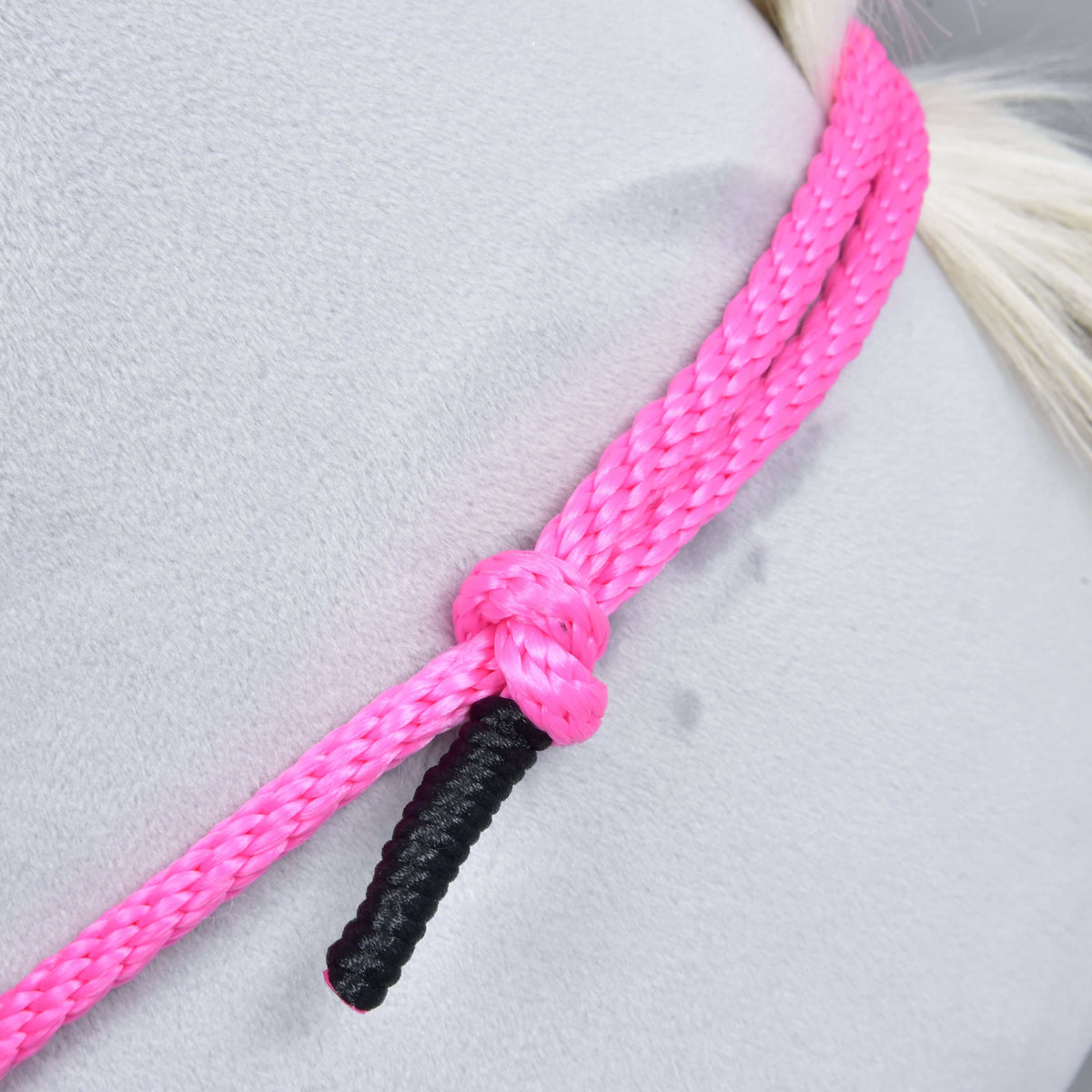 Close-up of the pink braided rope of Cordeo Pink Festive with a knot and black wrapped end on a grey plush neck