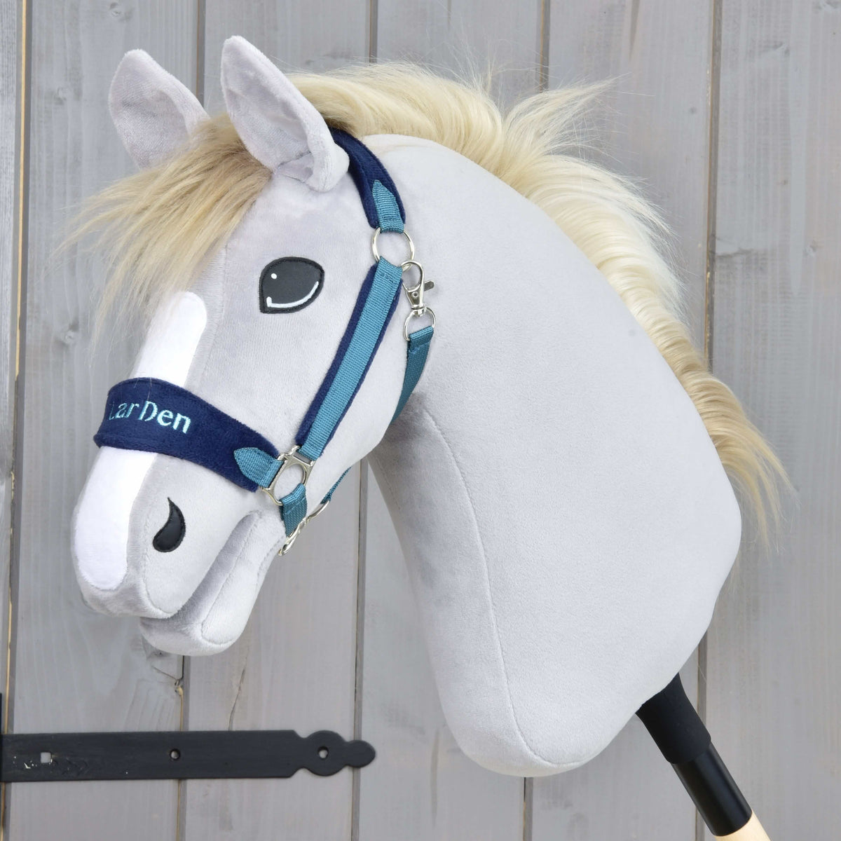 Szürke plüss Hobby Horse ló krémszínű sörénnyel a kék szőrmés kötőfékben, a sötétkék orrszíjon LarDen hímzéssel