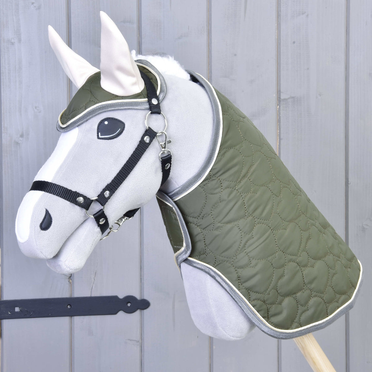 Az Olivetti szett egy szürke plüss Hobby Horse lovon: olívazöld steppelt takaró és fülvédő krémszínű fülekkel, fekete kötőfék