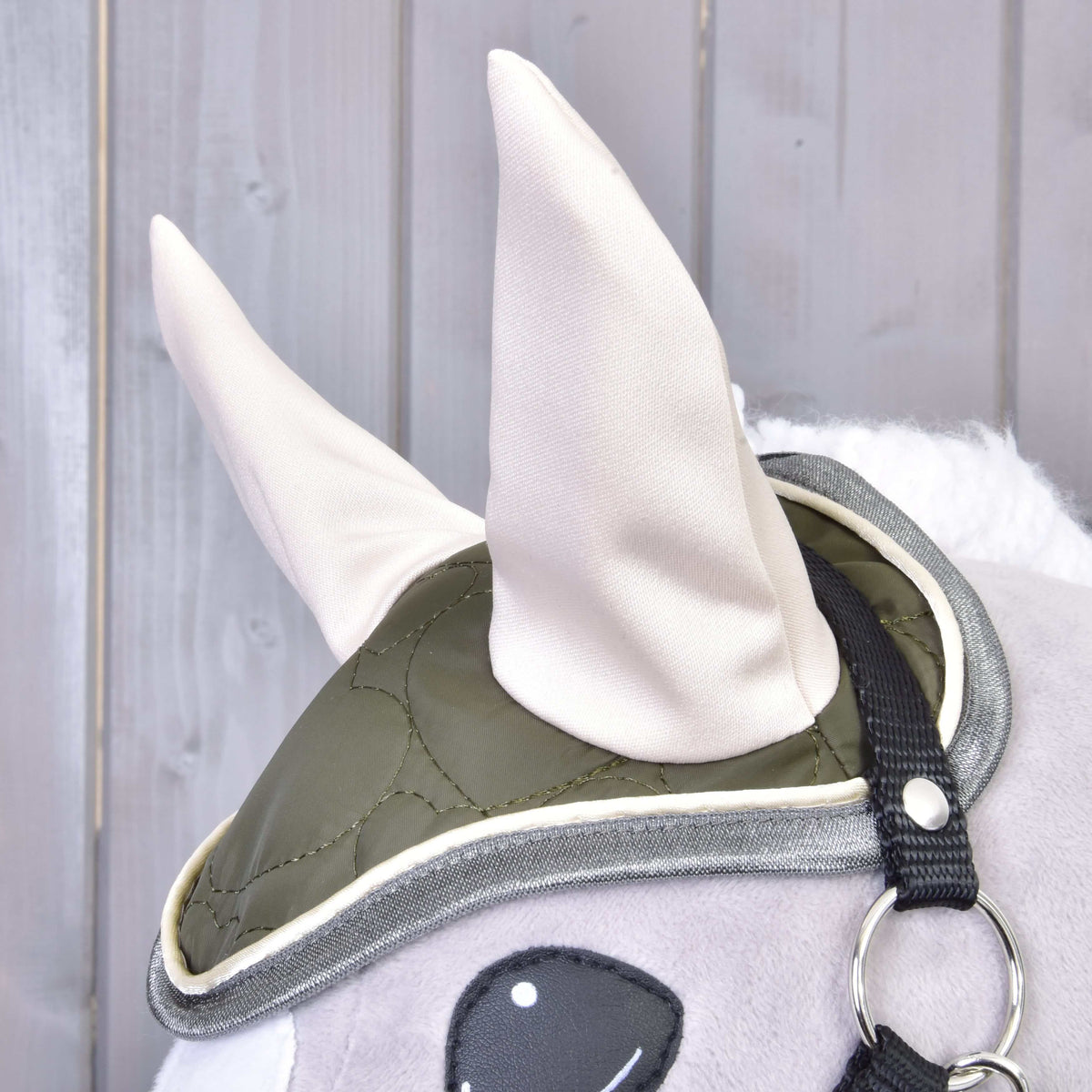 Az Olivetti szett olívazöld steppelt fülvédője közelről krémszínű fülekkel és szürke paszpóllal egy szürke Hobby Horse lovon