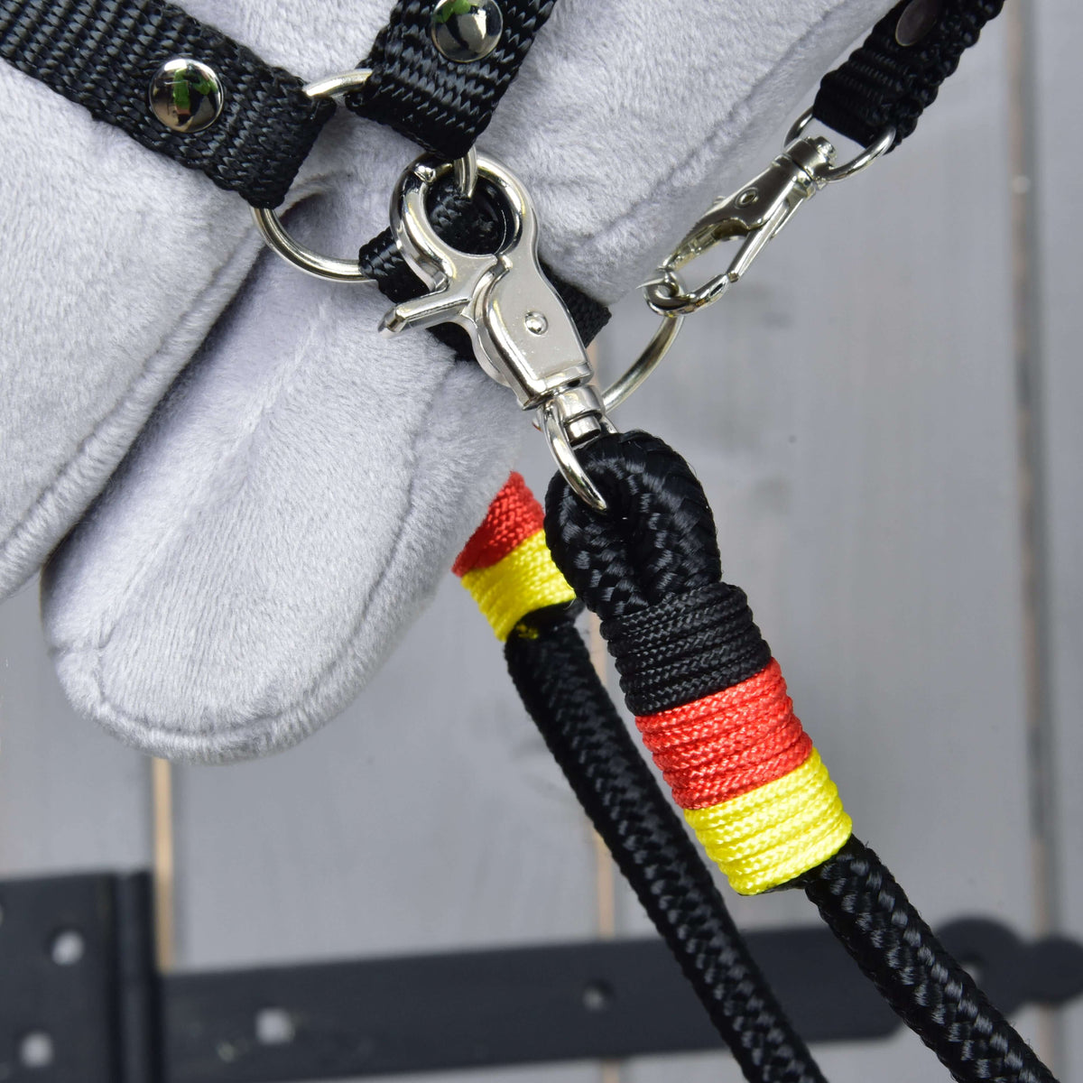 Close-up of the Reins Emblem snap hook clipped to the halter ring, with yellow and red wraps on the black rope