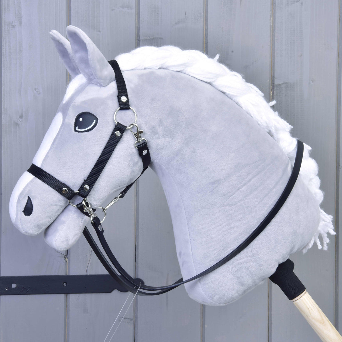 Black leatherette reins clipped to the black halter of a light grey Hobby Horse with a braided white mane