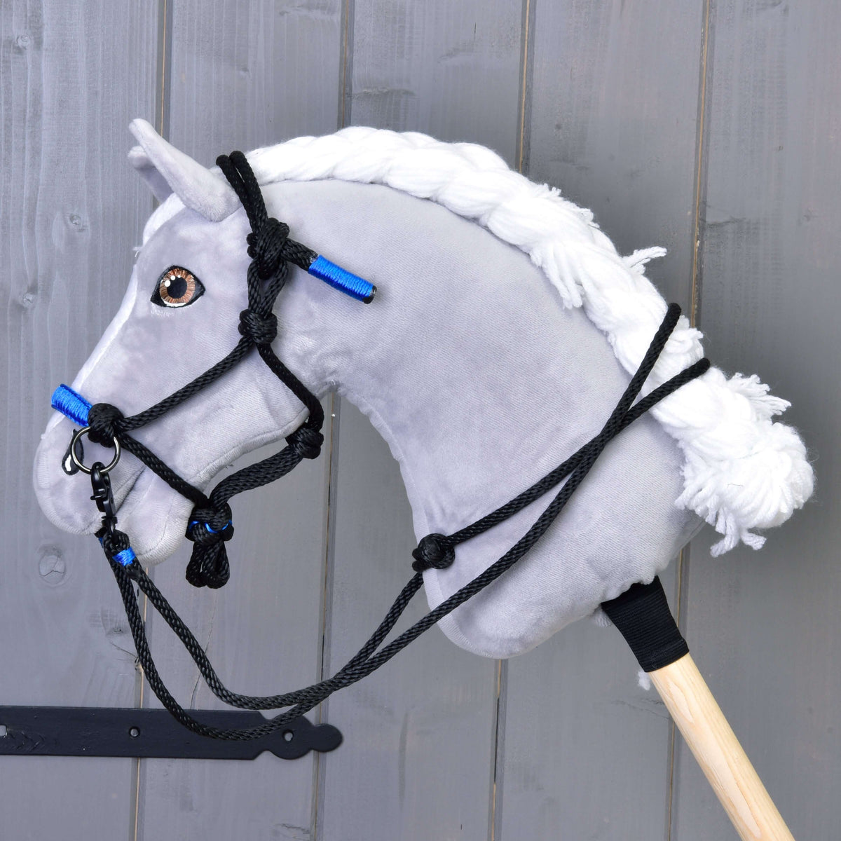 Szürke plüss Hobby Horse ló fonott fehér sörénnyel, rajta a fekete-kék csomózott kötőfék és fekete kötél kantárszár