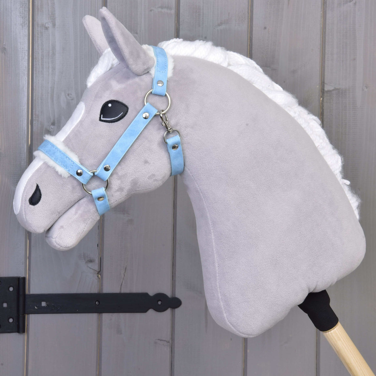 Szürke Hobby Horse ló bal profilból a Pastell Blue szőrmés műbőr kötőfékben, amelynek szíjait fehér szőrme béleli
