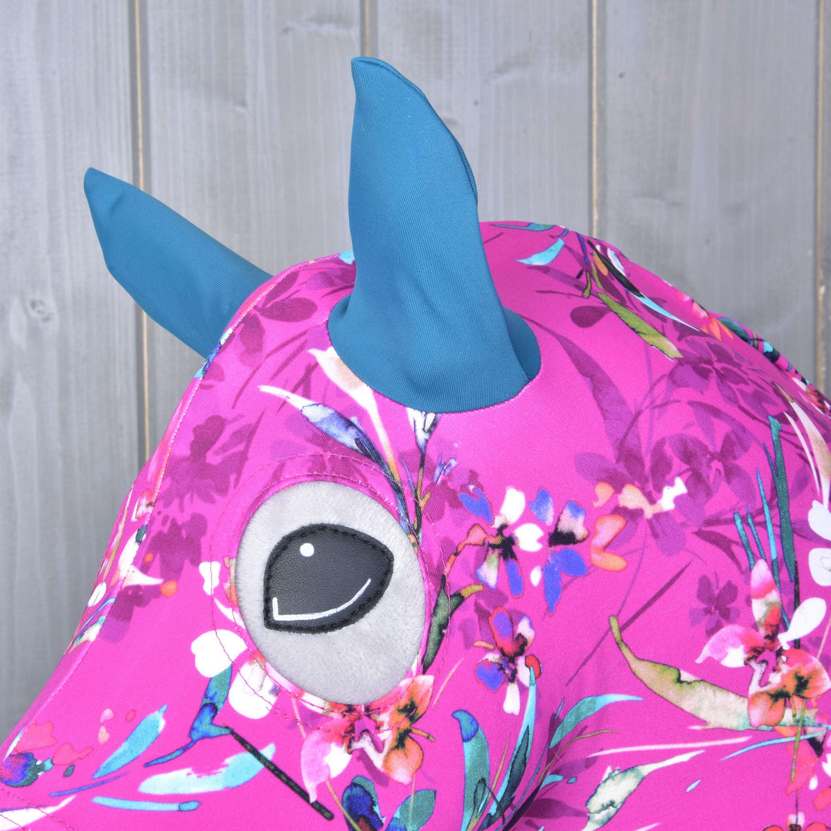 A kékeszöld fülek és a szemnyílás közelről a fehér és korallszínű virágokkal díszített magenta Lycra anyagon egy szürke Hobby Horse lovon