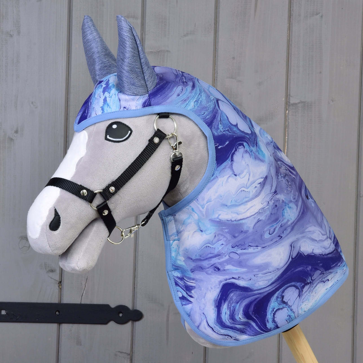 Szürke Hobby Horse ló fekete kötőfékben, rajta a Galaxy Blue esőtakaró kék-lila márványos mintával és kékesszürke fülekkel