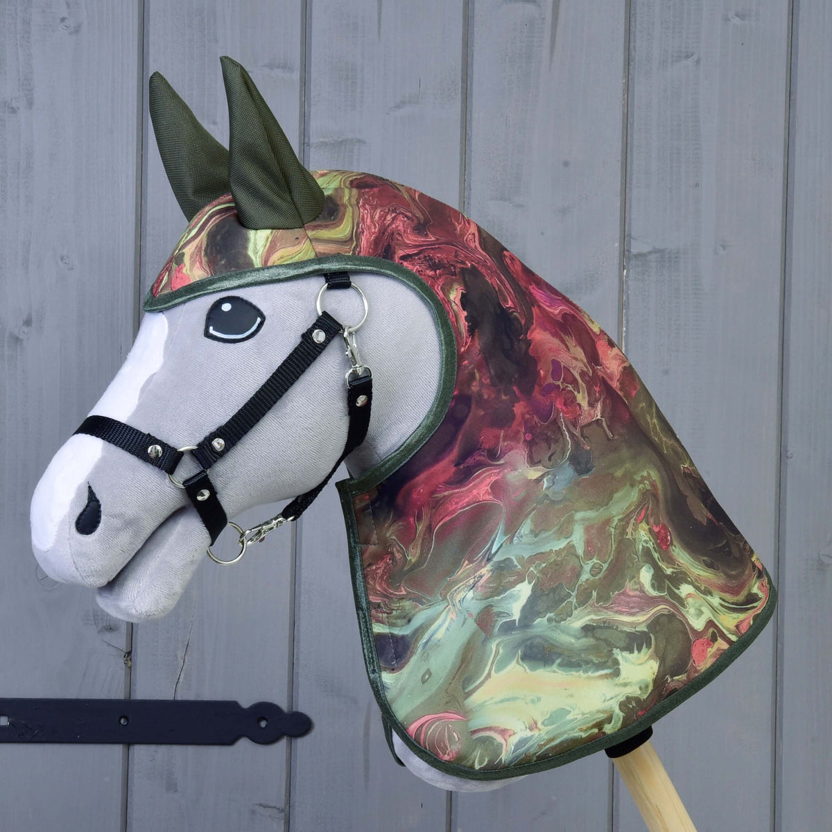 A grey plush Hobby Horse in a black halter wears the Raincoat Galaxy with marbled red and green print and olive ears