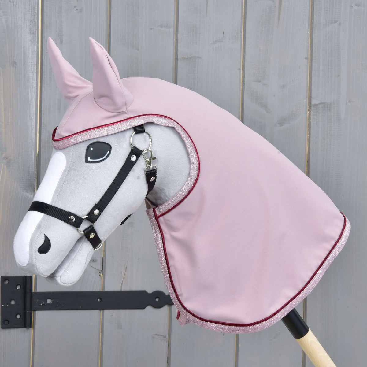 Világosszürke Hobby Horse ló fekete kötőfékben, a fáradt rózsaszín Veloria esőtakaróban kapucnival, fülekkel és csillámos szegéllyel