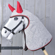 Szürke Hobby Horse ló fekete kötőfékben, a fején és nyakán melírozott szürke esőtakaró piros fültakarókkal