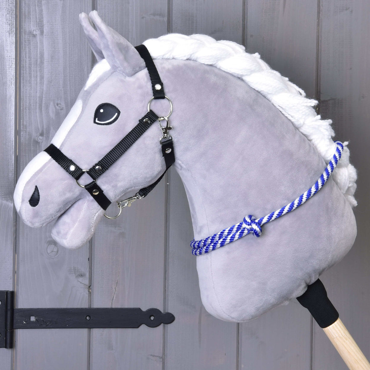 Szürke Hobby Horse ló fekete kötőfékben, a nyakán a kék-fehér csíkos kötél nyakgyűrű (cordeo)
