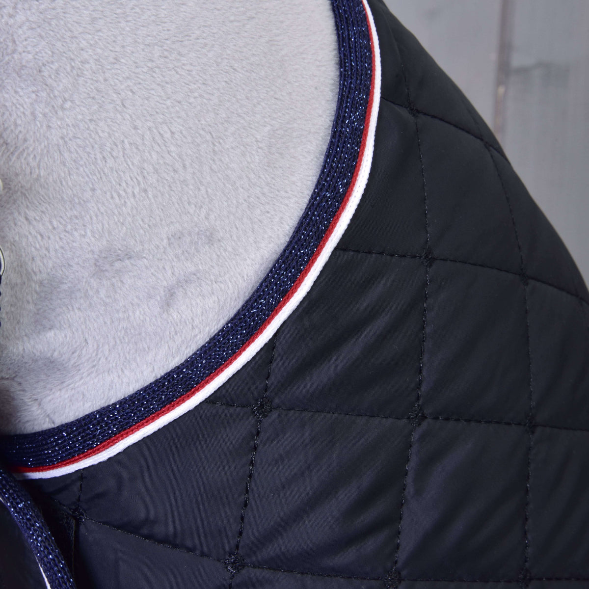 Detail of the diamond quilting and navy glitter, red and white striped edging of the black blanket at the neck