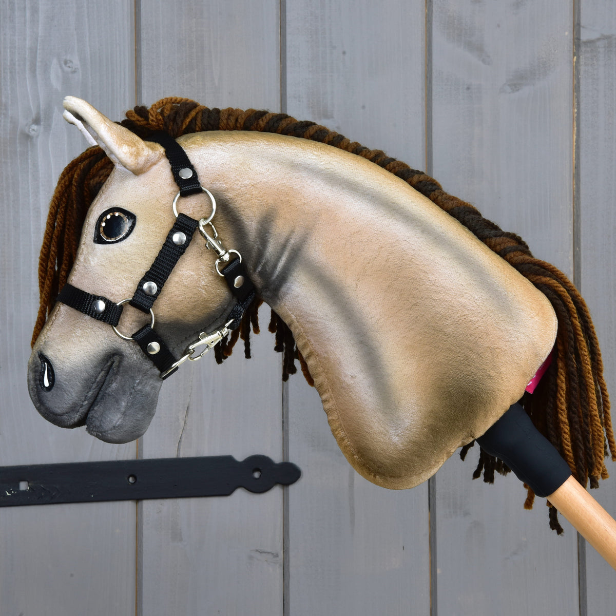 Side view of Hobby Horse Ruby showing the shaded beige plush neck and brown yarn mane against a grey wooden door