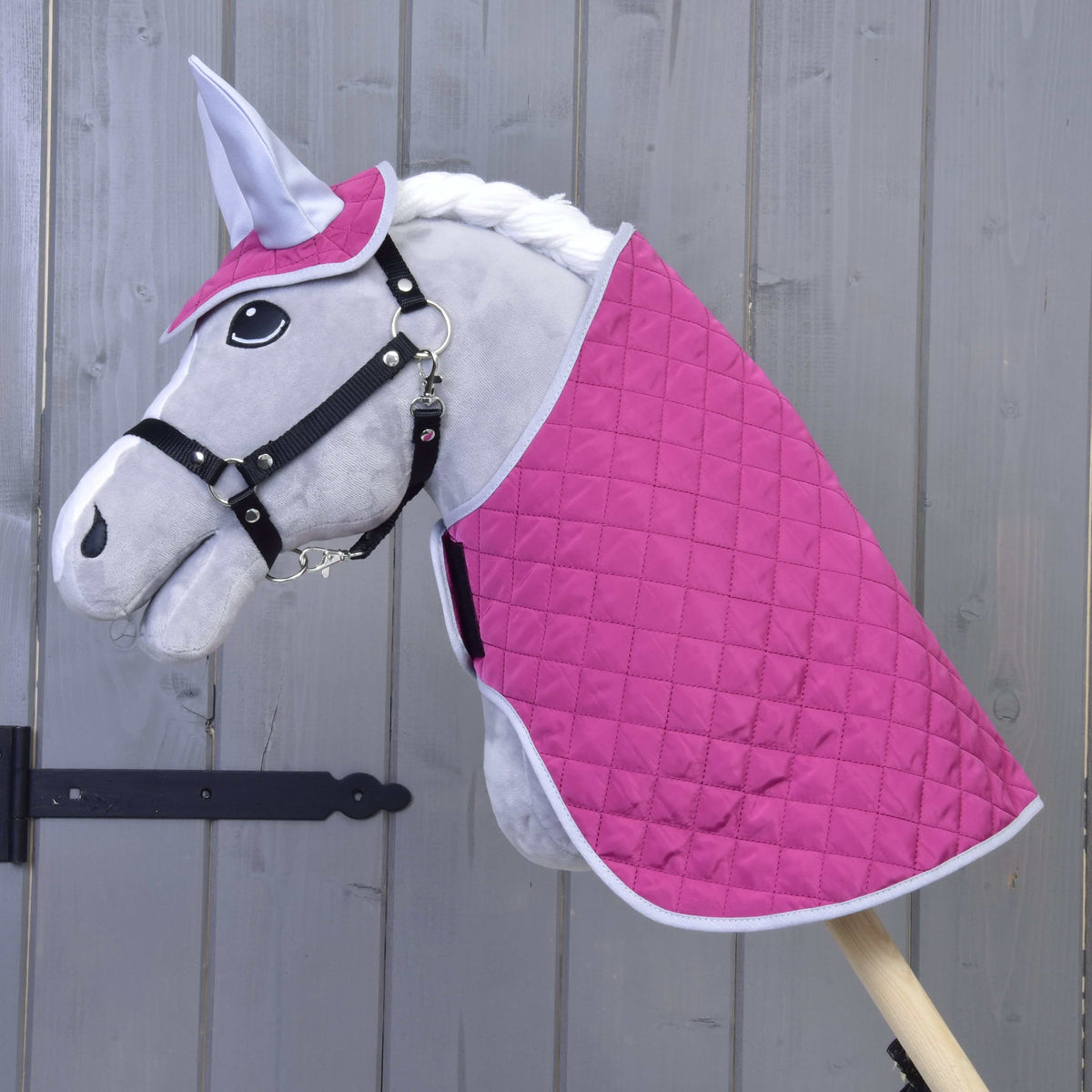 Grey Hobby Horse in a black halter wearing the quilted hot pink blanket and ear bonnet with silver ears
