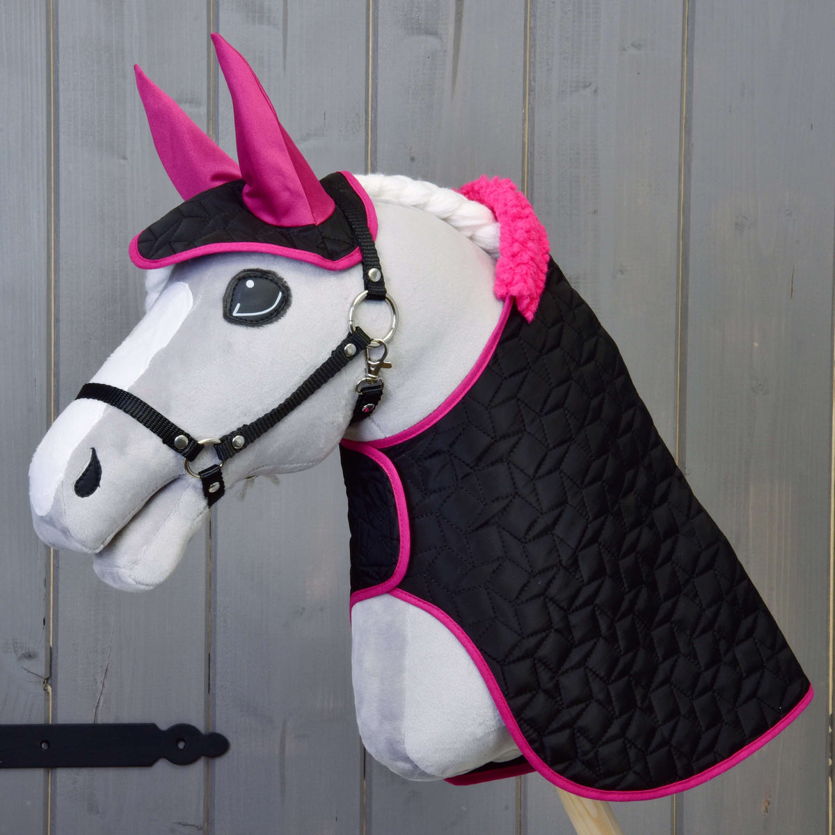 Grey Hobby Horse in a black halter wearing the quilted black blanket with pink fur collar and the ear bonnet with pink ears