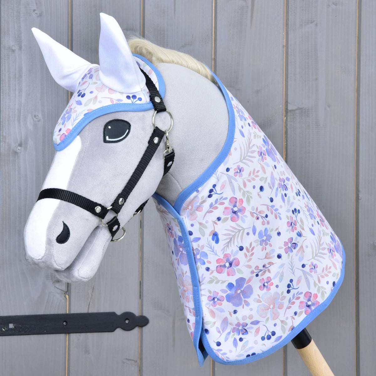 Világosszürke Hobby Horse ló fekete kötőfékkel, a virágmintás takaróban és a hozzáillő fülvédőben fehér fülrészekkel és kék szegéllyel