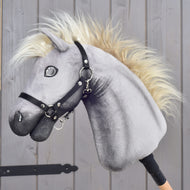 LarDen Hobby Horse Silver Dream szürke plüssfejjel, krémszínű sörénnyel és fekete kötőfékkel, oldalról, egy fa istállóajtó mellett