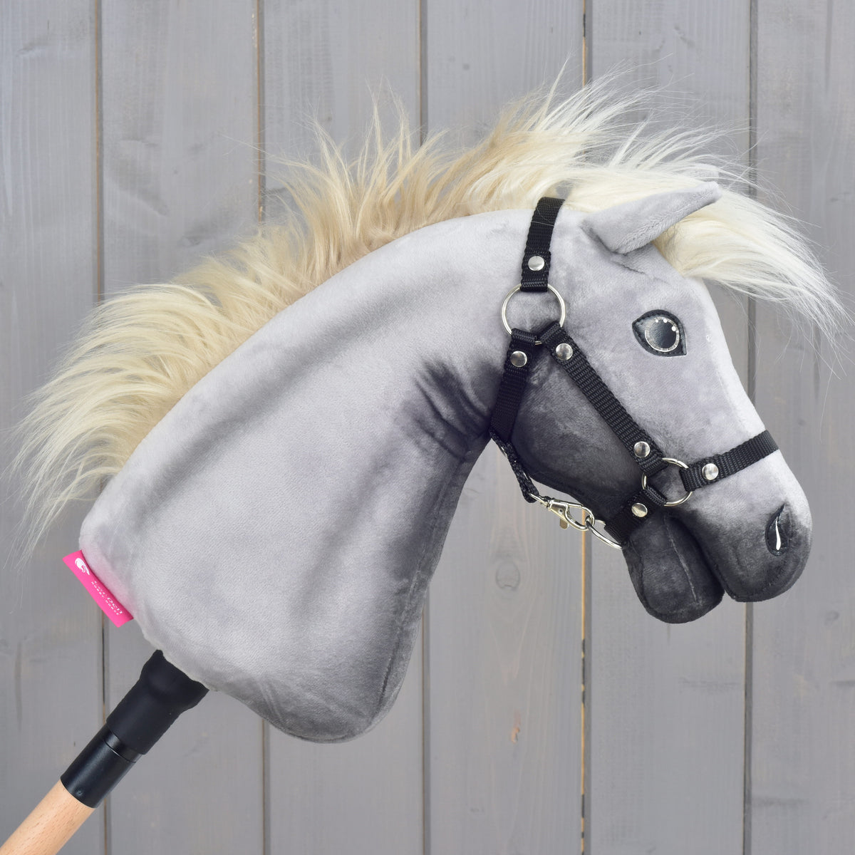 A Silver Dream Hobby Horse ló jobb profilból: szürke plüssfej, fekete kötőfék és rózsaszín címke a faboton