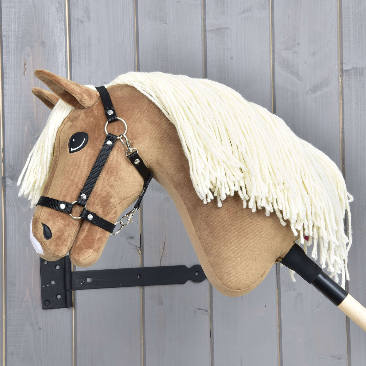 Hobby Horse Smart in left profile with a long cream yarn mane over the neck and a black halter, against grey wood