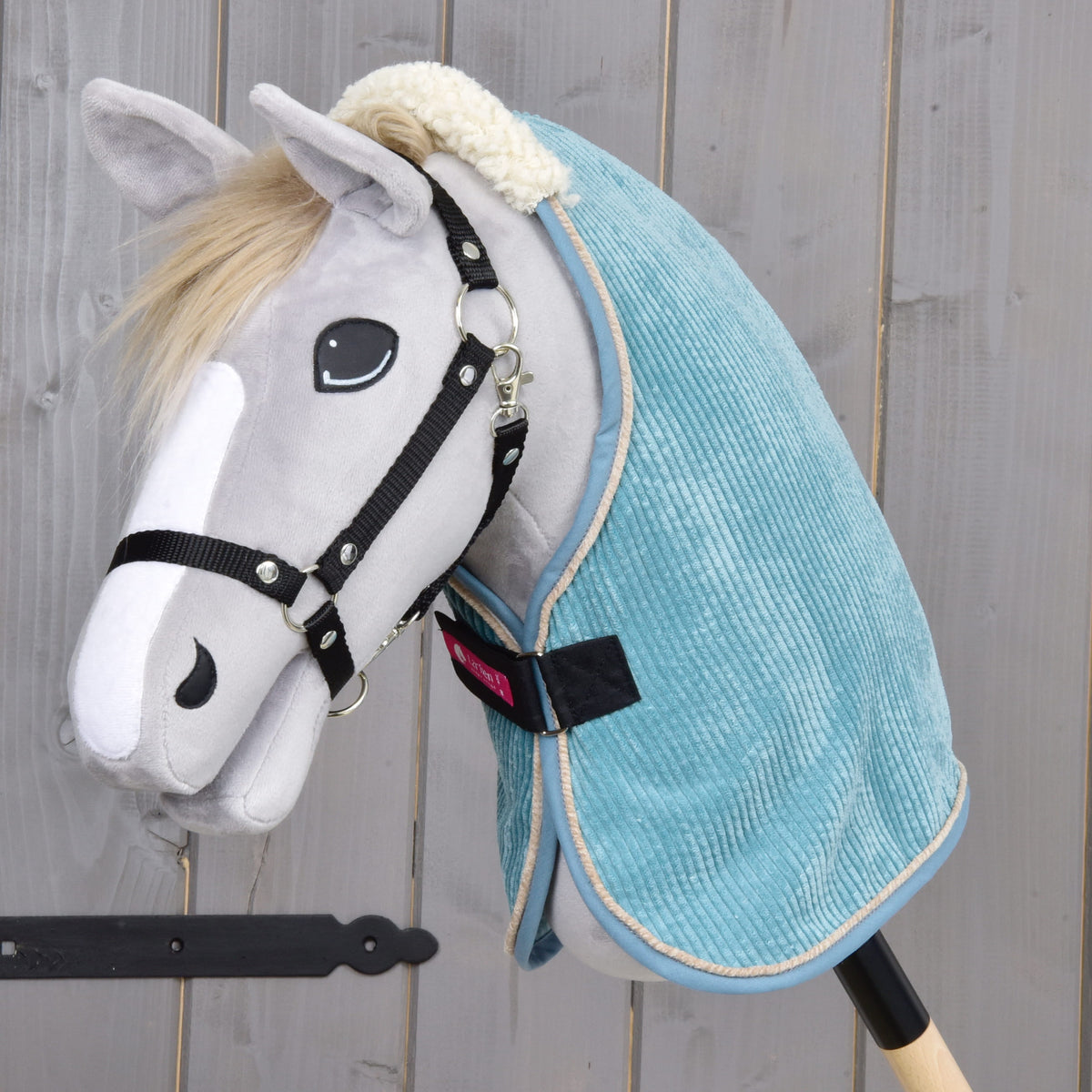 Világosszürke Hobby Horse ló fekete kötőfékkel, a krémszínű teddy gallérú kékeszöld kordbársony istállótakaróban