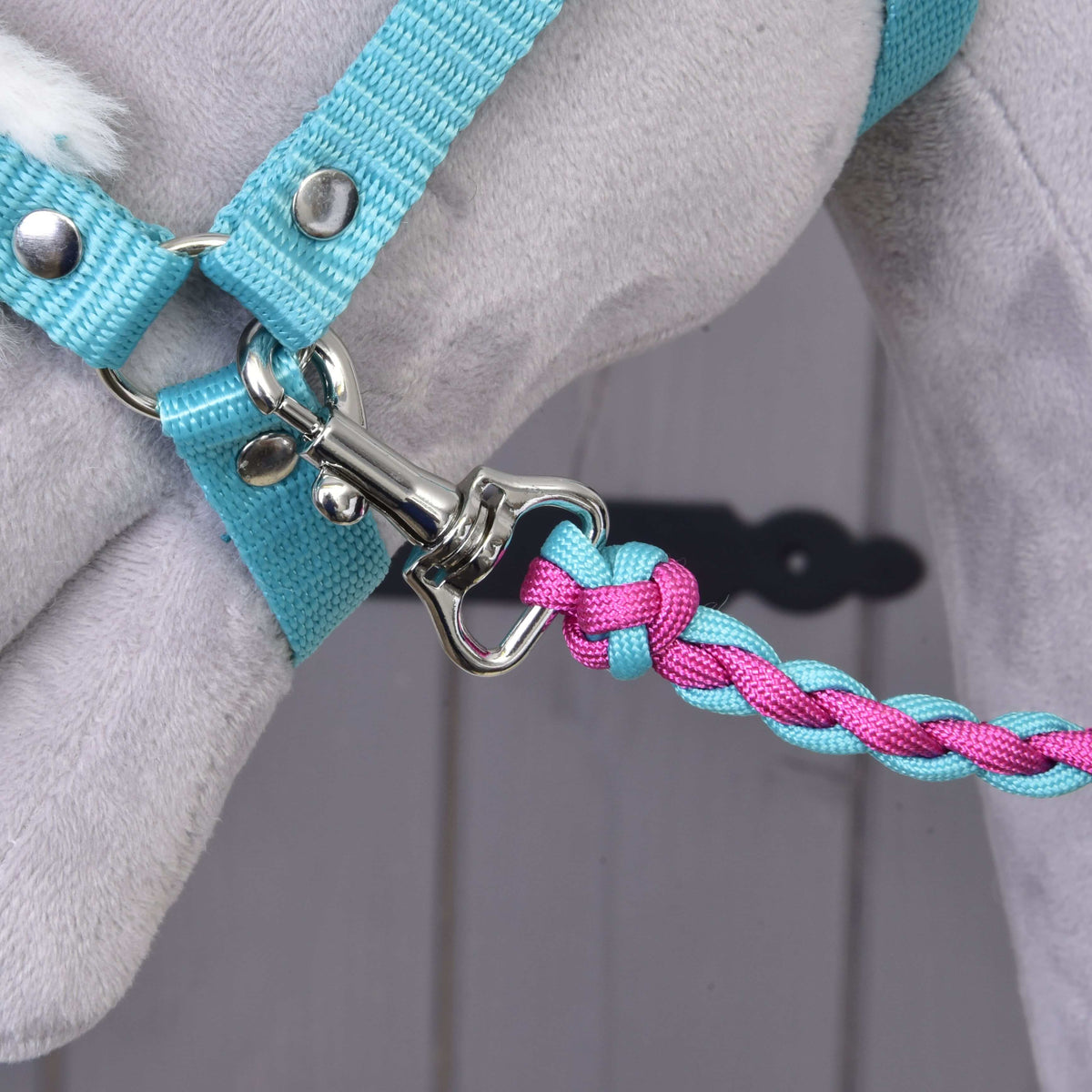 Ezüst karabiner, amely a türkiz kötőféket egy fonott rózsaszín-türkiz kötélhez kapcsolja egy szürke Hobby Horse lovon
