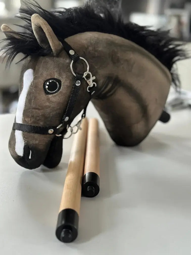 Barna Hobby Horse fej fekete sörénnyel, fehér hókával és fekete kötőfékkel egy kétrészes, fekete végű fabot mellett