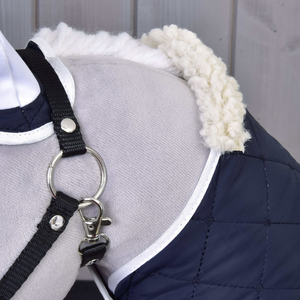 Close-up of the cream fleece collar and white-trimmed navy quilted blanket on the shoulder of a grey Hobby Horse