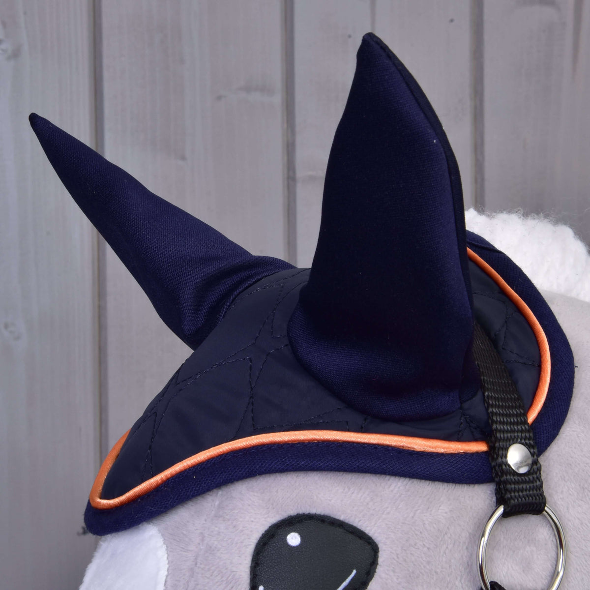 A sötétkék fülvédő közelről magas sötétkék fülekkel és narancssárga paszpóllal egy szürke Hobby Horse lovon