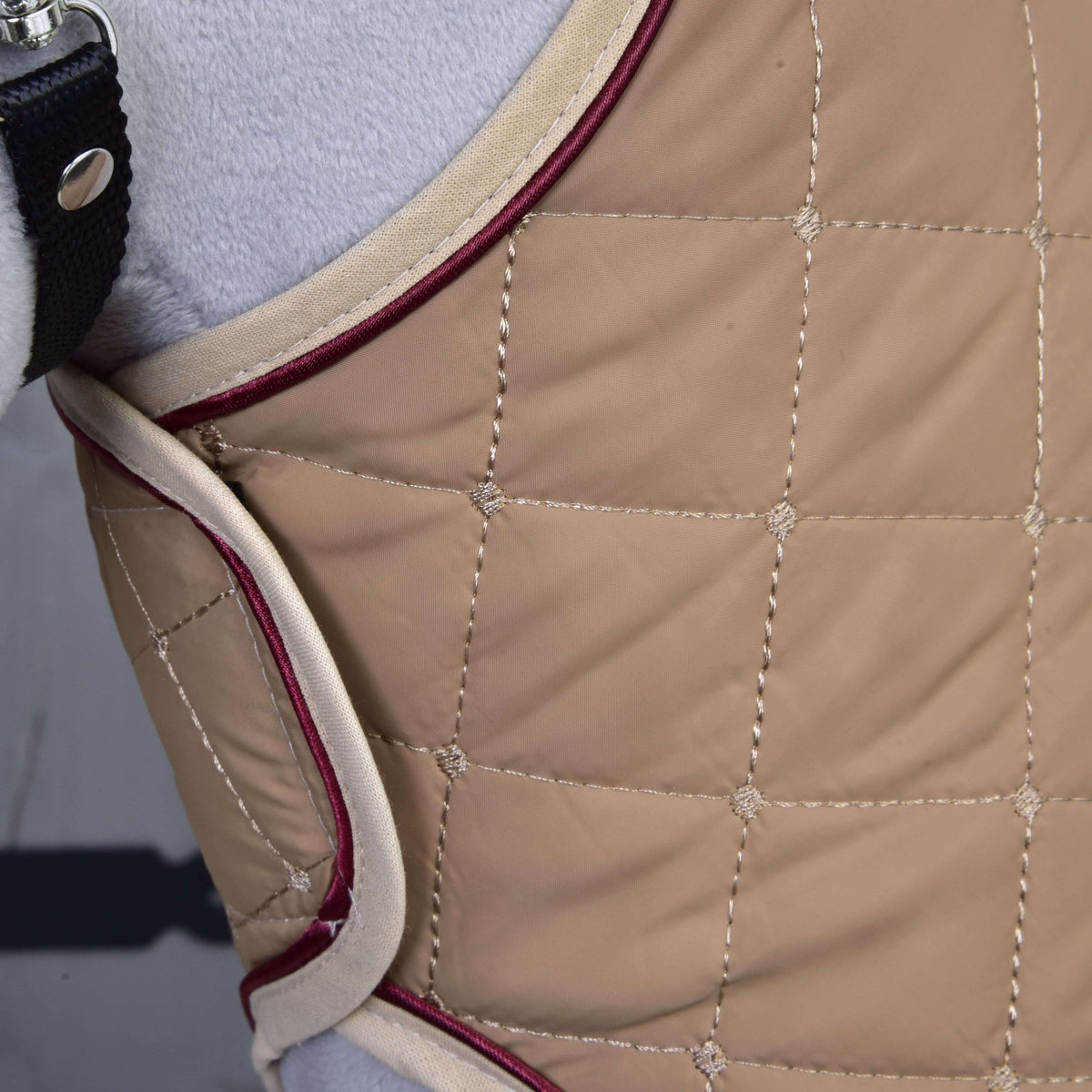 Close-up of the beige blanket with square quilting, cream edging and burgundy piping on a grey Hobby Horse