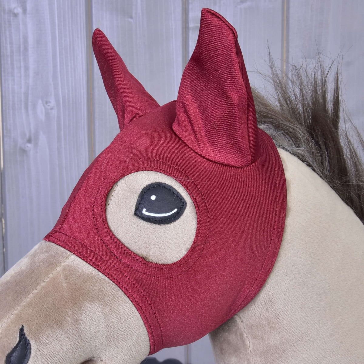 Közeli kép: a sötétpiros Barn Red maszk egy bézs Hobby Horse lovon, mindkét fül hegyes fülrészben, a szemet tűzés keretezi
