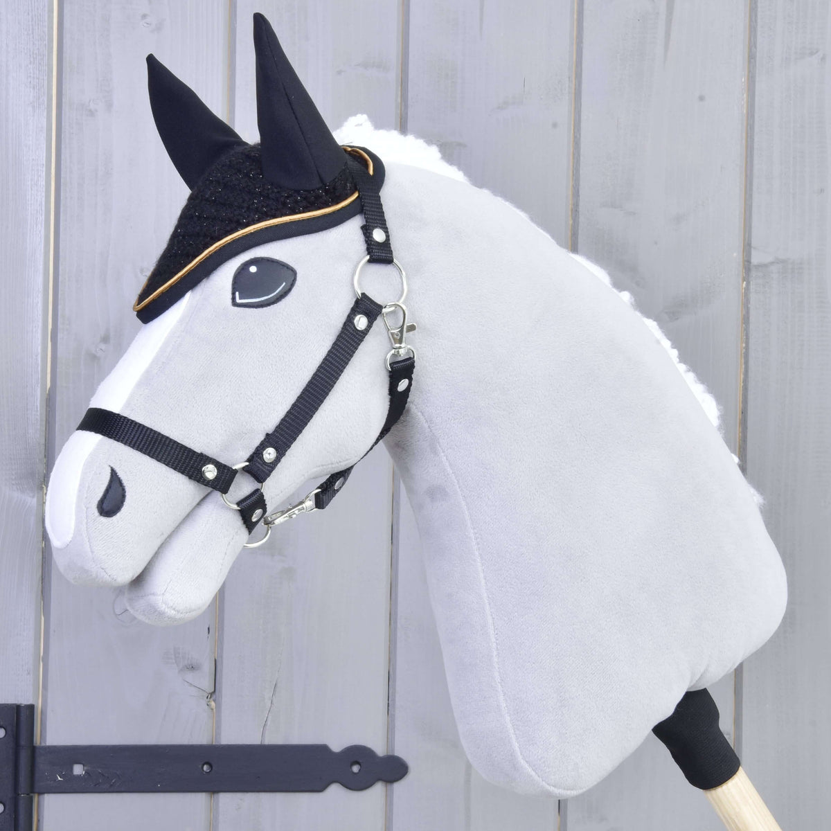 Fehér szőrmesörényű szürke Hobby Horse ló fekete kötőfékkel és az arany szegélyű fekete horgolt fülvédővel