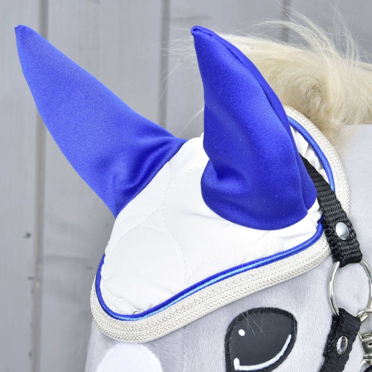 Close-up of the Ear Bonnet Cream Pearl on a grey Hobby Horse: royal blue ears, cream quilting and a glittery silver edge