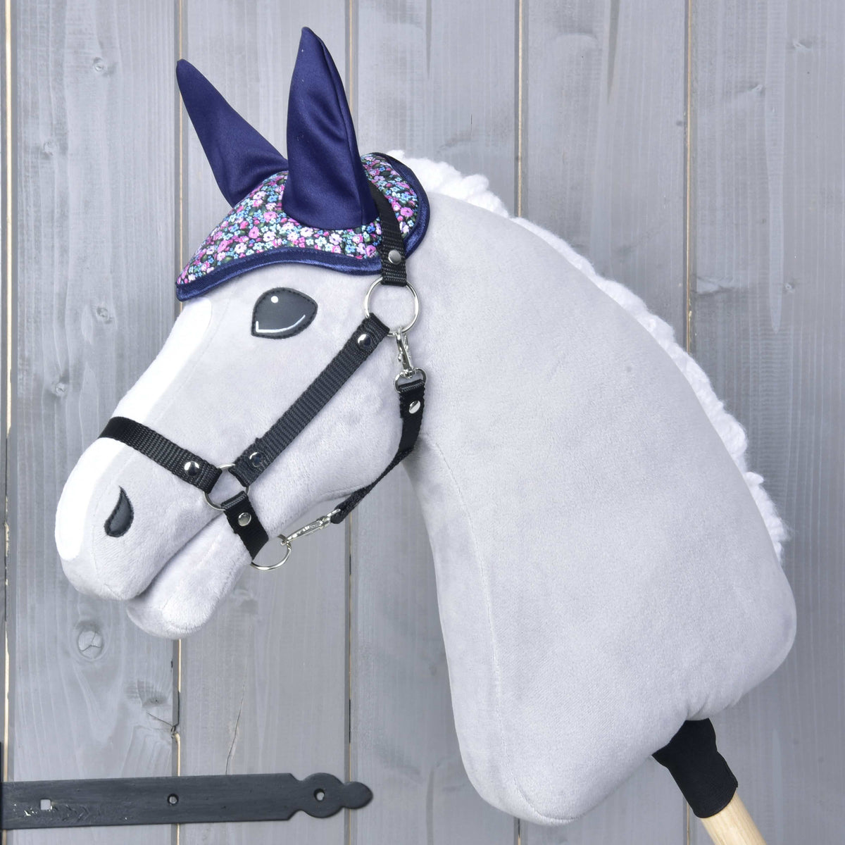 Szürke Hobby Horse ló fekete kötőfékben, sötétkék fülvédőben, amelynek apró virágmintája a homlokán húzódik