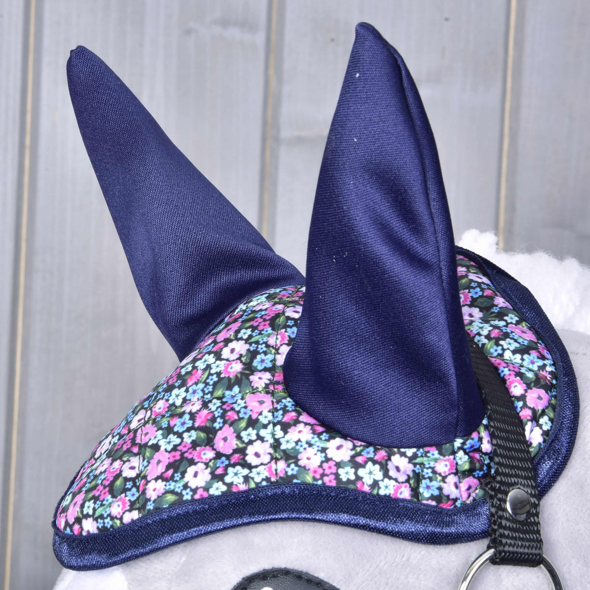 A sötétkék fülek és a virágmintás steppelt fejrész közelről, sötétkék szegéllyel, egy szürke Hobby Horse ló fején