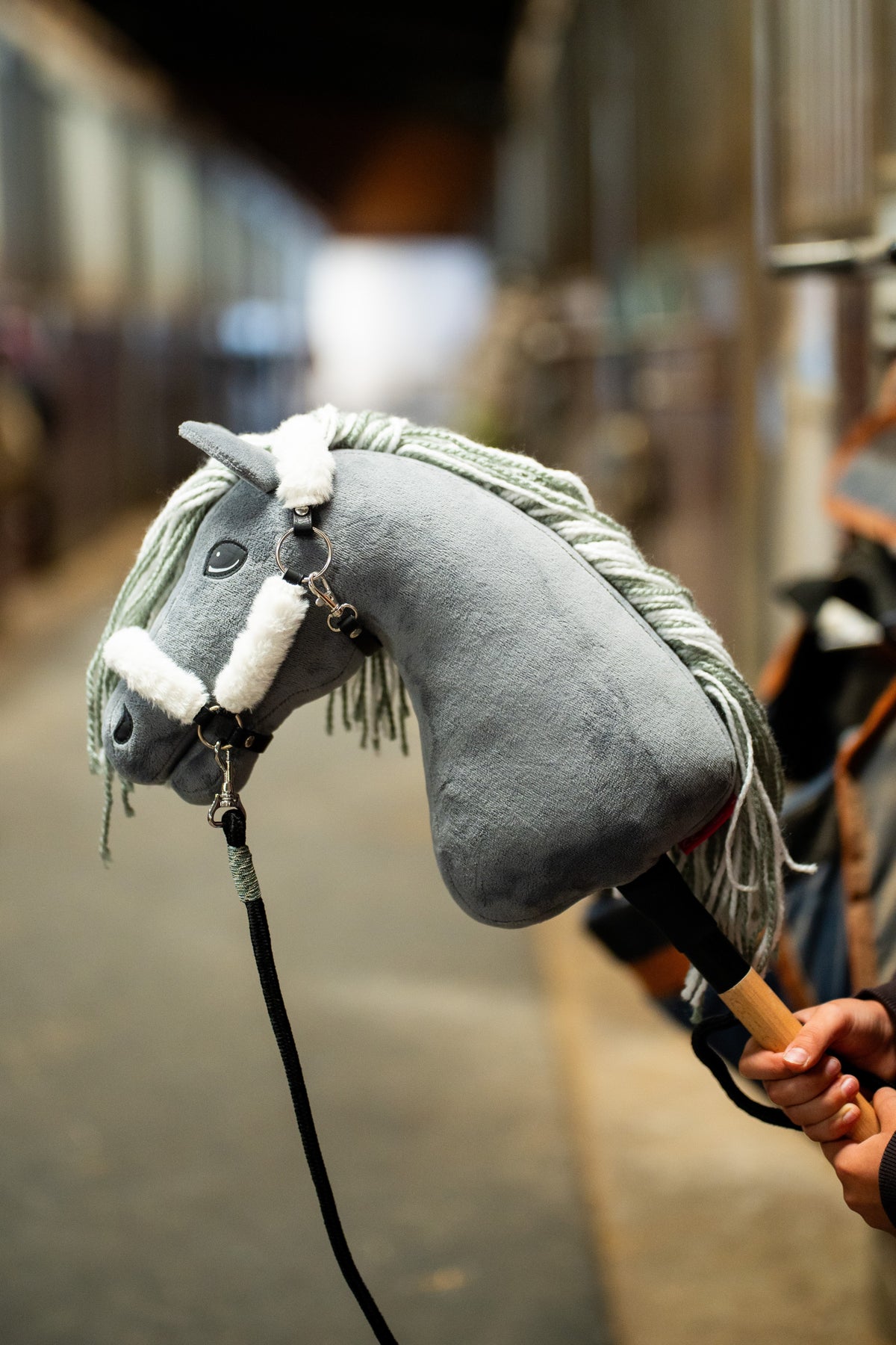 Közeli kép a Hobby Horse Calypso lóról fehér szőrmés kötőfékben, puha szőrmével az orrszíjon és a tarkószíjon, fekete vezetőszárral