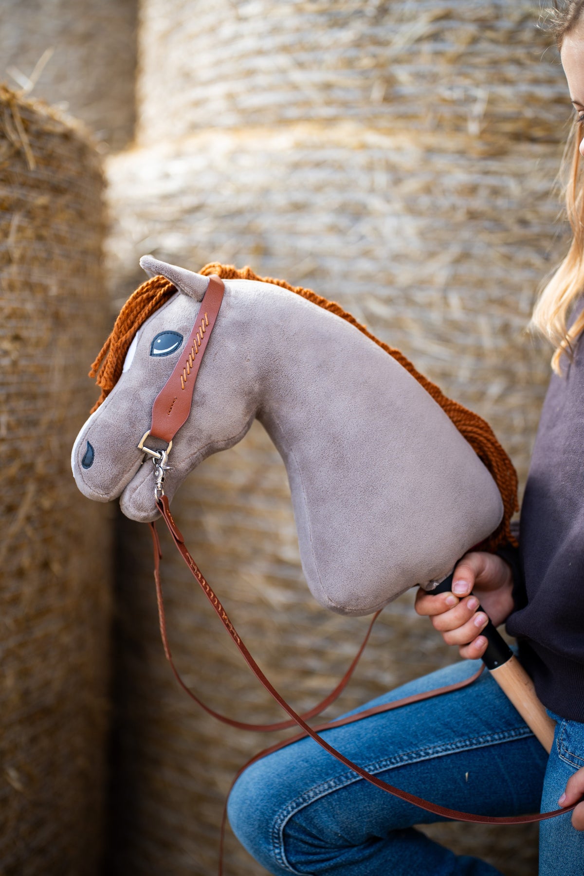 Hobby Horse Chanell up close in a brown bridle with gold stitching and long brown reins, held in front of straw bales