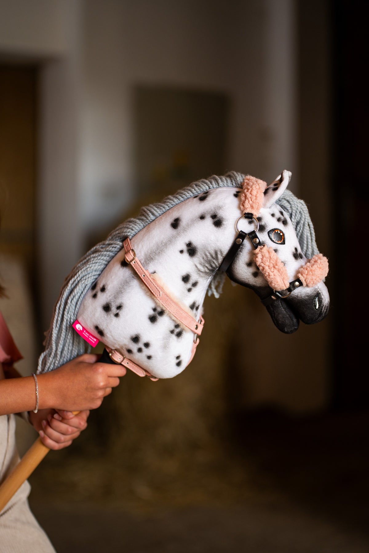 Hobby Horse Chantal közelről barackrózsaszín szőrmés kötőfékben és púderrózsaszín szügyelőben, fehér nyakán fekete foltokkal